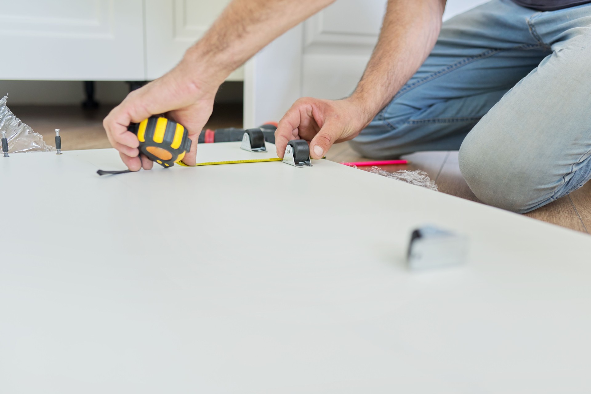 Montaje de muebles blancos de madera en casa, manos de carpintero con herramientas y cinta métrica